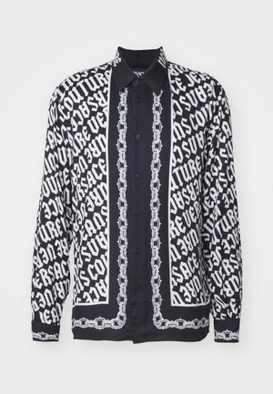 Čierno-bielá košeľa s dlhým rukávom, ktorá obsahuje výrazné textové vzory a detaily v tvare reťaze, so klasikou golierom a gombíkovým zapínaním.