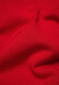 Nahaufnahme von rotem Strickstoff, der die detaillierte Textur und das feine Rippmuster mit sanften Falten und Schatten zeigt.