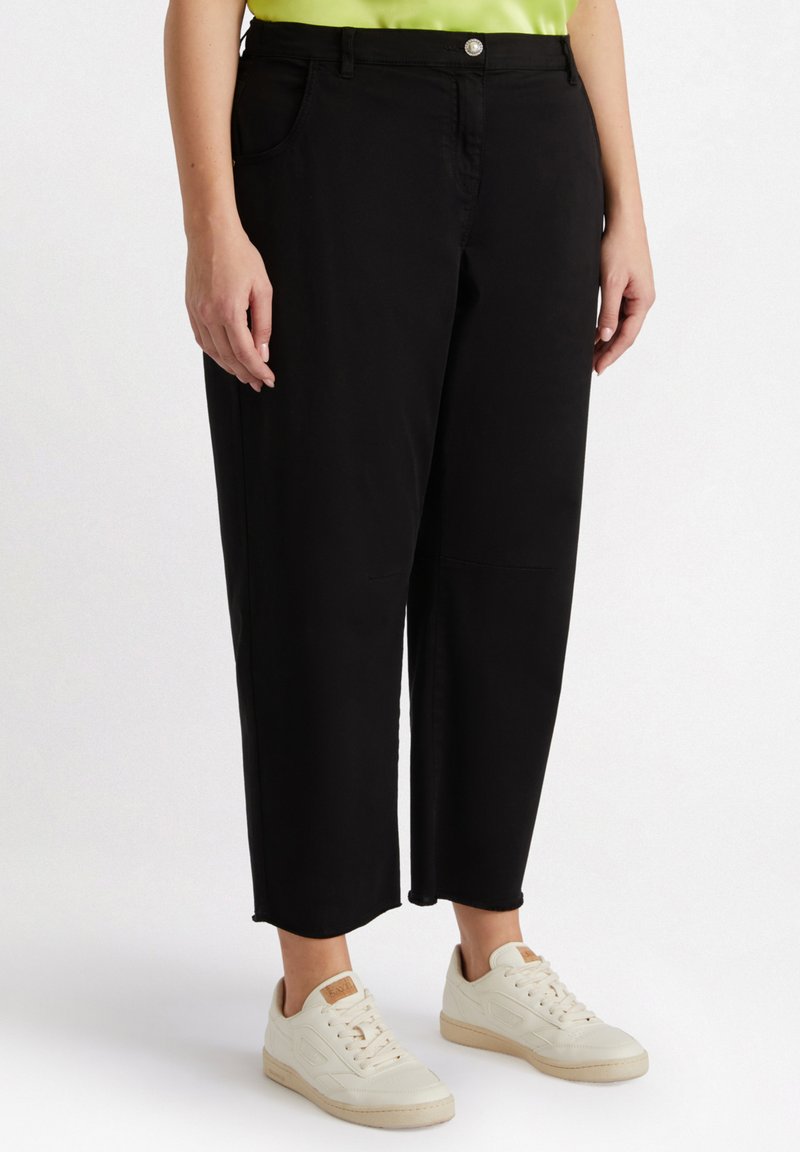 Czarne wycięte spodnie wykonane z miękkiego materiału, charakteryzujące się klasycznym wzorem z przednimi kieszeniami i zapięciem na guzik, zestawione z białymi trampkami.