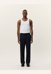 Hvit tanktopp og marineblå bukser, glatt stoff, rett ben-design, minimalistisk stil, sammen med mørke sko, sett fra front.