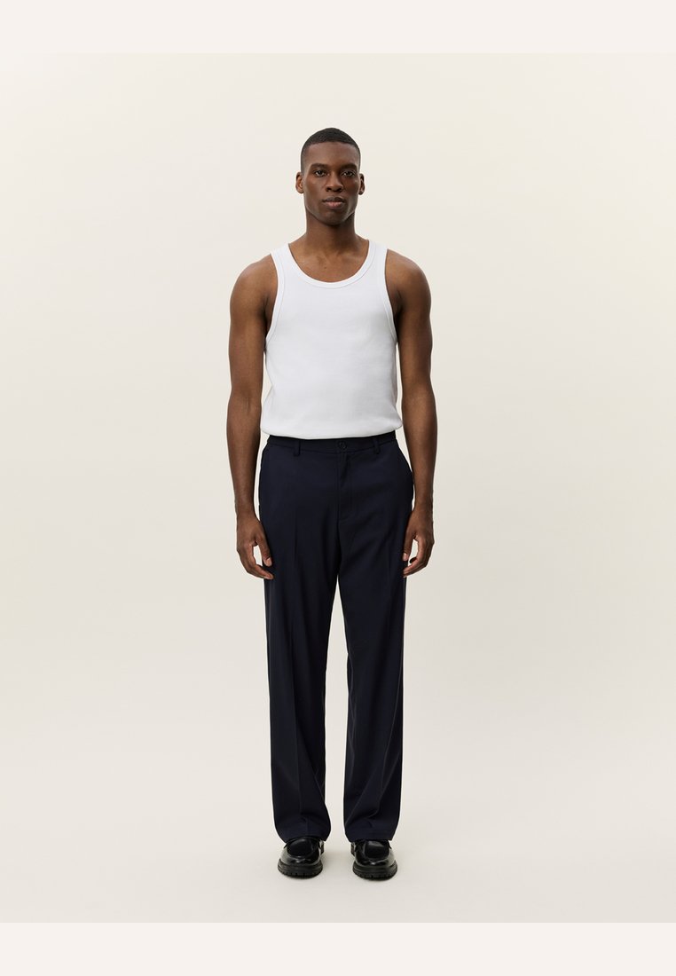 Hvit tanktopp og marineblå bukser, glatt stoff, rett ben-design, minimalistisk stil, sammen med mørke sko, sett fra front.