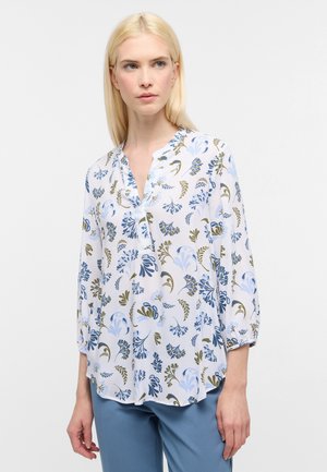 Witte blouse met een blauw en groen bloemenpatroon, lange mouwen en een ontspannen pasvorm, met een kraag en knoopdetail.
