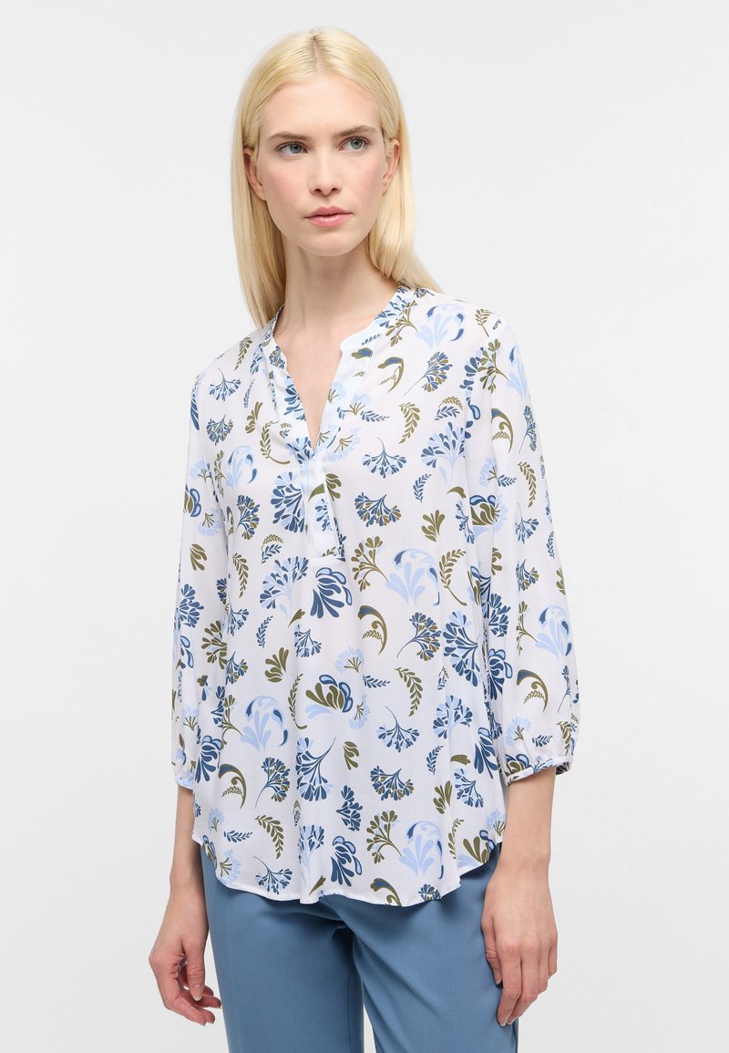 Weiße Bluse mit blauem und grünem Blumenmuster, langen Ärmeln und einem lässigen Schnitt, ausgestattet mit einem Kragen und Knopfdetails.