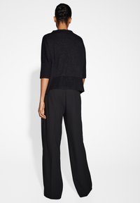 Pull en maille noire à coupe décontractée et manches courtes. Associé à un pantalon large noir, avec une texture de tissu lisse.