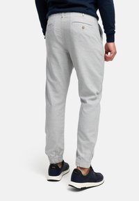 Pantalones jogger en gris claro, confeccionados con un material suave, que cuentan con puños elásticos y dos bolsillos traseros con detalles de botones, combinados con zapatillas deportivas en color marino.