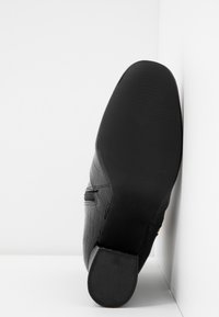 Svart lädersko med strukturerad yta, spetsig tå och gummisulor, med en låg klack och subtila sömnadsdetaljer.