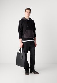 Felpa nera con cappuccio interno grigio chiaro e tasca frontale, abbinata a jeans neri e borsa tote in pelle nera. Le scarpe sono sneakers scure.