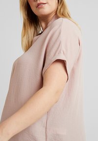 Maglietta rosa chiaro a maniche corte con un tessuto morbido e strutturato. Presenta una vestibilità rilassata e un collo rotondo, evidenziando dettagli di design sottili.