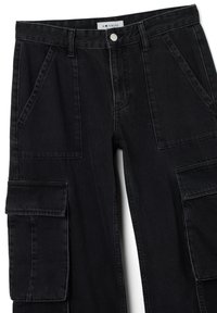 Pantalones cargo negros de denim, con múltiples bolsillos, cierre de botón y corte recto. La textura tiene un ligero desgaste.