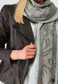 Veste grise en similicuir avec épaules matelassées, fermeture éclair noire ; écharpe bleu clair avec motif floral gris et texture douce.