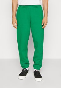 Grønne sweatpants med elastisk talje og manchetter. Har et struktureret logo-print på venstre ben. Bæres med sorte sneakers.