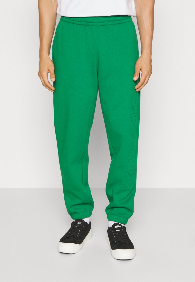 Grønne sweatpants med elastisk talje og manchetter. Har et struktureret logo-print på venstre ben. Bæres med sorte sneakers.