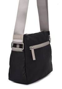 Bolso de hombro negro de nylon con una correa ajustable gris, bolsillo con cremallera en la parte frontal y etiqueta del logo KCB. Textura suave y forma rectangular.
