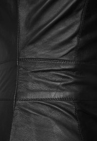 Tissu en cuir noir présentant une texture lisse avec des plis subtils. Comprend des coutures surpiquées et des motifs de grain variés sur toute la surface.