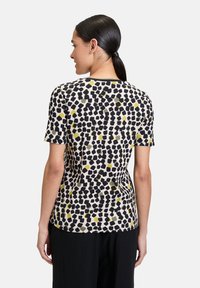 T-shirt à manches courtes en tissu doux avec un motif abstrait noir, jaune et vert sur un fond clair, et un col rond.