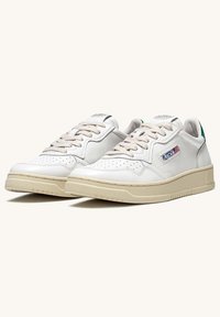 Sneaker bianche in pelle con suole in gomma beige, dotate di lacci beige, design perforato, accent green sul tallone e un logo sul lato.