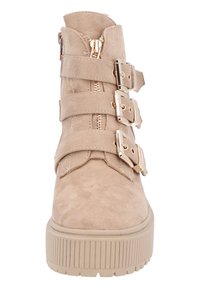 Beige mockasins stövletter med tre metallspännen, en dragkedjedetalj och en räfflad plattformssula. Slät yta med rundad tå.