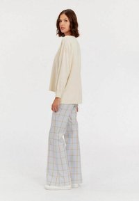 Pull en tricot crème, coupe ample avec des manches longues, associé à un pantalon large à carreaux bleu clair et orange. Des baskets blanches complètent le look.