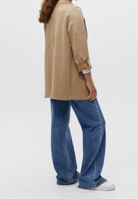 Beige tailored jacket with rolled cuffs, paired with high-waisted blue denim wide-leg jeans, complemented by white sneakers.