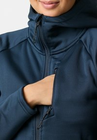 Marineblauwe hoodie met rits van een gladde stof, voorzien van een hoge kraag en zakken. De rits heeft een trekker voor gemakkelijke toegang.