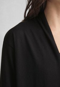 Svart v-ringad topp i mjukt stickat material, med en avslappnad passform och slät textur. Lagerkragen avslöjar en subtil drapering.