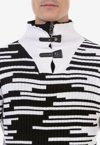 Gestrickter Pullover in Schwarz und Weiß mit einem hohen Kragen, geometrischem Muster, Reißverschluss und Lederakzenten am Hals.