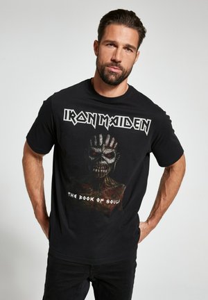 T-shirt en coton noir avec un imprimé graphique d'un visage squelettique et le texte "Iron Maiden - The Book of Souls" en blanc. Manches courtes.