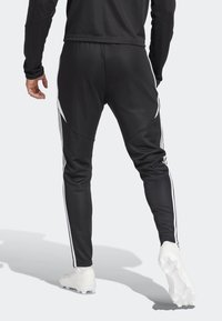 Svarta atletiska byxor i ett slätt tyg, med vita sidostycken och en avsmalnande passform, elastisk midja och texturerade detaljer.