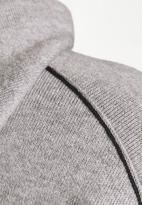 Szary dzianinowy hoodie z teksturowanej tkaniny, z wysokim kołnierzem i szwem biegnącym wzdłuż ramienia dla dodatkowego detalu w designie.