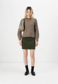Brun strikket genser med bølget kant, kombinert med et grønt kordfløyelskjørt. Tilbehør inkluderer en beige veske med slangeskinnmønster og svarte loafers.