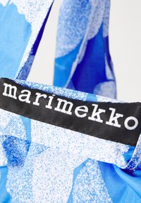 Blue fabric tote bag with abstract patterns in various shades of blue. Features a black label with white text, "marimekko."