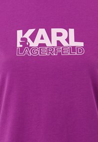 Camiseta de algodón morada con gran texto blanco que dice "KARL LAGERFELD" y un gráfico de perfil. Textura suave con un corte relajado.
