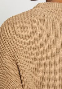 Pull tricoté de couleur beige clair avec un motif côtelé texturé et un col rond, mettant en valeur des coutures et des finitions détaillées.