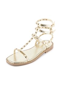 Sandaler gladiator med remme, metallic guld finish, flad sål, dekorative pyramide nitter og lagdelte remme med spænde accenter.