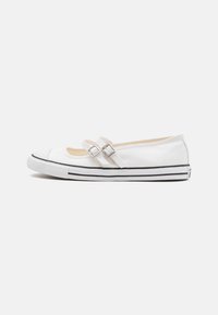 Zapatillas Mary Jane de lona blanca con correas doble hebilla y suela de goma a rayas negras sobre fondo blanco liso.