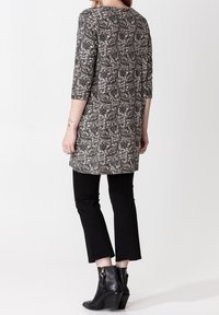 Černobílá tunika s paisley vzorem a tříčtvrtečními rukávy, spárovaná s černými zkrácenými kalhotami a černými koženými kotníkovými botami na podpatku.