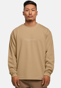 Felpa beige con vestibilità rilassata, dotata di scollatura rotonda e maniche lunghe. Presenta un discreto logo bianco sul davanti e polsini a costine.