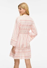 Robe rose à motifs avec des manches longues et une taille élastique. Présente des motifs géométriques en ivoire et en nuances de corail. Ourlet évasé.