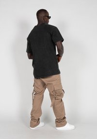 Sort bomulds-t-shirt med korte ærmer, parret med brune cargobukser med lommer og snore. Hvide sneakers fuldender outfittet.