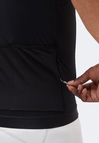 Το χέρι τραβά μικρό φερμουάρ στην κάτω πίσω τσέπη ενός μαύρου υφασμάτινου αθλητικού μπλουζιού.