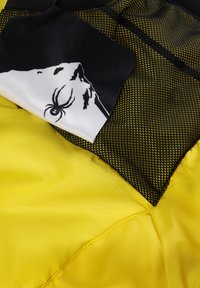 Gelbes Gewebe mit glatter Textur; schwarzer Netzakzent; weißes Gewebe mit einer Grafik eines Wesens, das eine Spinne und eine Felsenillustration zeigt.