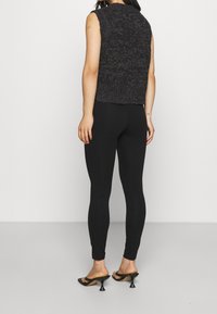 Top in maglia senza maniche di colore grigio con finitura testurizzata, abbinato a leggings neri e sandali neri con tacco a punta.