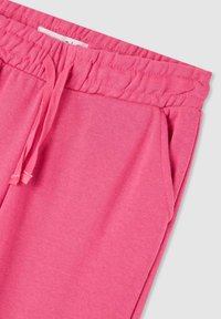 Pantaloni della tuta rosa con vita elastica e coulisse. Presentano tasche laterali e un tessuto morbido e testurizzato. Design casual orientato al comfort.