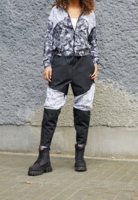 Černobílá květinová bunda na zip s kontrastními vzorovanými rukávy, kombinovaná s černými kalhotami s paisley akcenty a černými bojovými botami.