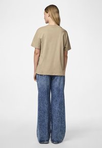 Μπεζ βαμβακερό t-shirt με κοντά �μανίκια, συνδυασμένο με φαρδιά τζιν παντελόνια μπλε απόχρωσης, που διαθέτουν φθαρμένη υφή και κλασικές ραφές.