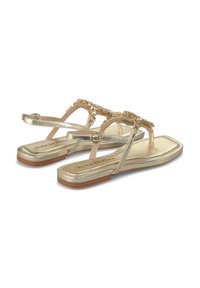 Sandali piatti metallici dorati con sottili cinturini e dettagli decorativi in perline. La suola è piatta ed è realizzata in gomma color marrone chiaro.