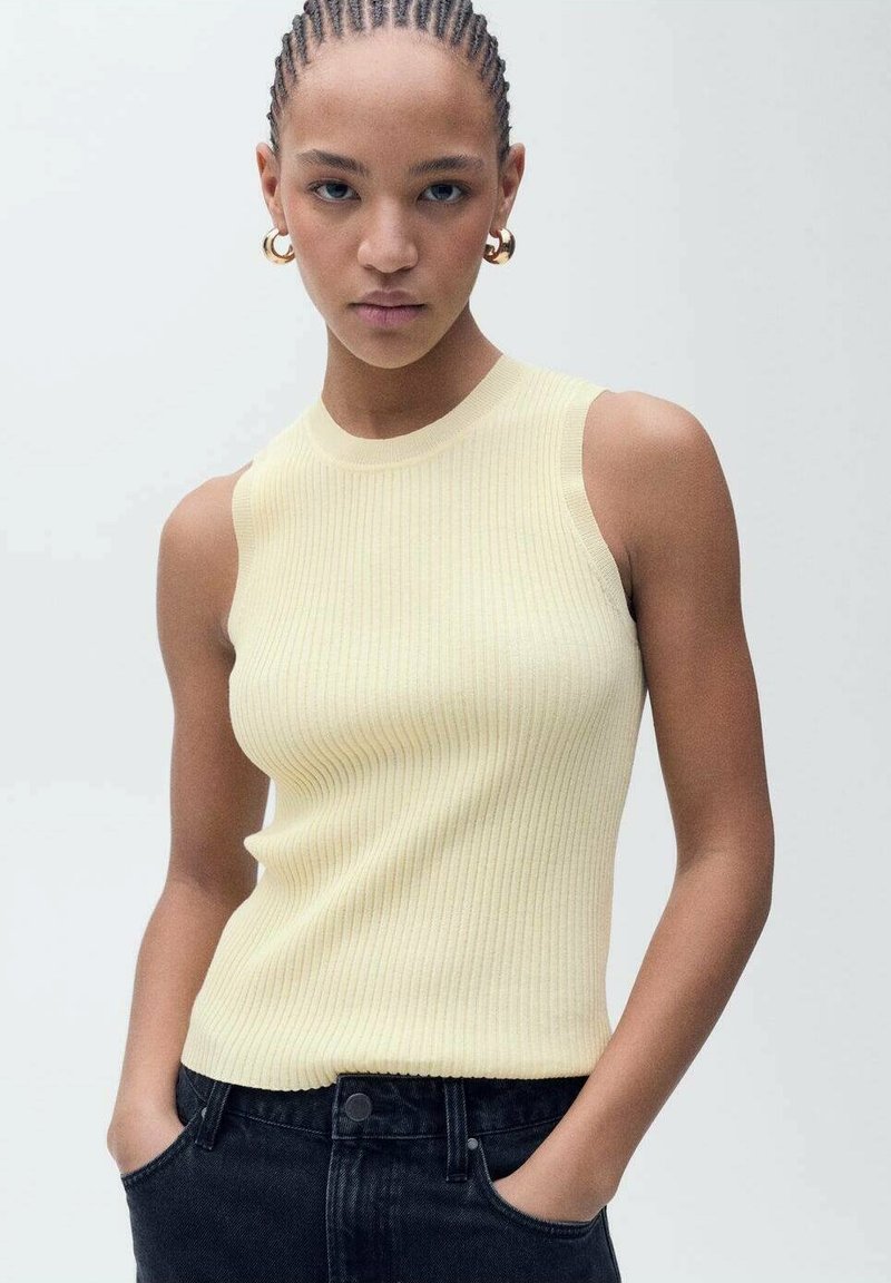 Žltý rebrovaný top bez rukávov z textúrovanej látky, skombinovaný s čiernymi jeansami vysokého pásu. Vyzeranie dopĺňajú bronzové kruhové náušnice.