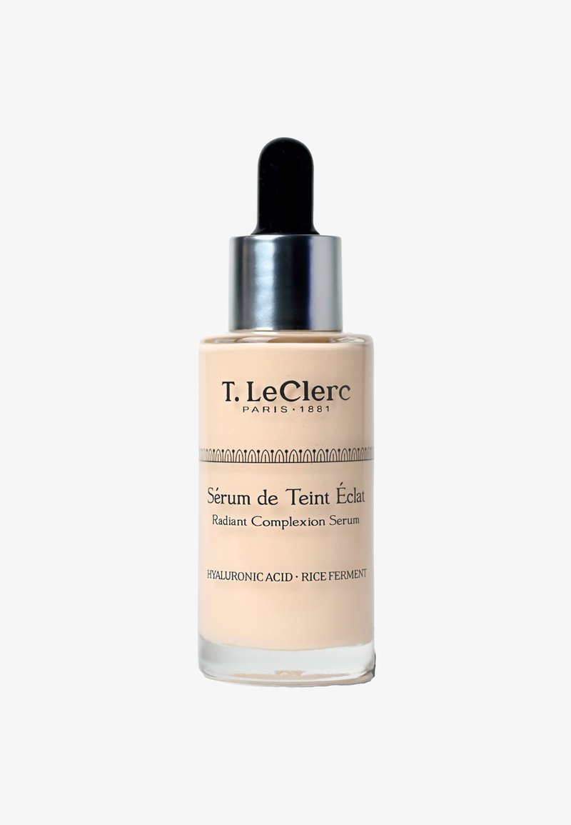 Flacon de sérum pour le teint éclatant T. LeClerc avec compte-gouttes, contenant de l'acide hyaluronique et un ferment de riz, liquide beige à l'intérieur.