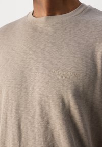 T-shirt girocollo beige chiaro in un tessuto morbido e testurizzato. Presenta un logo in rilievo "Marc O’Polo DENIM" sobrio sul davanti.