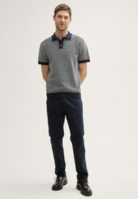 Polo à manches courtes rayé bleu marine et blanc avec col, associé à un pantalon sombre et des chaussures en cuir noires. Coupe régulière, détails côtelés.